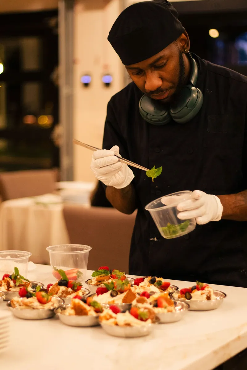 A chef plating berry desserts with tweezers at an evening gathering