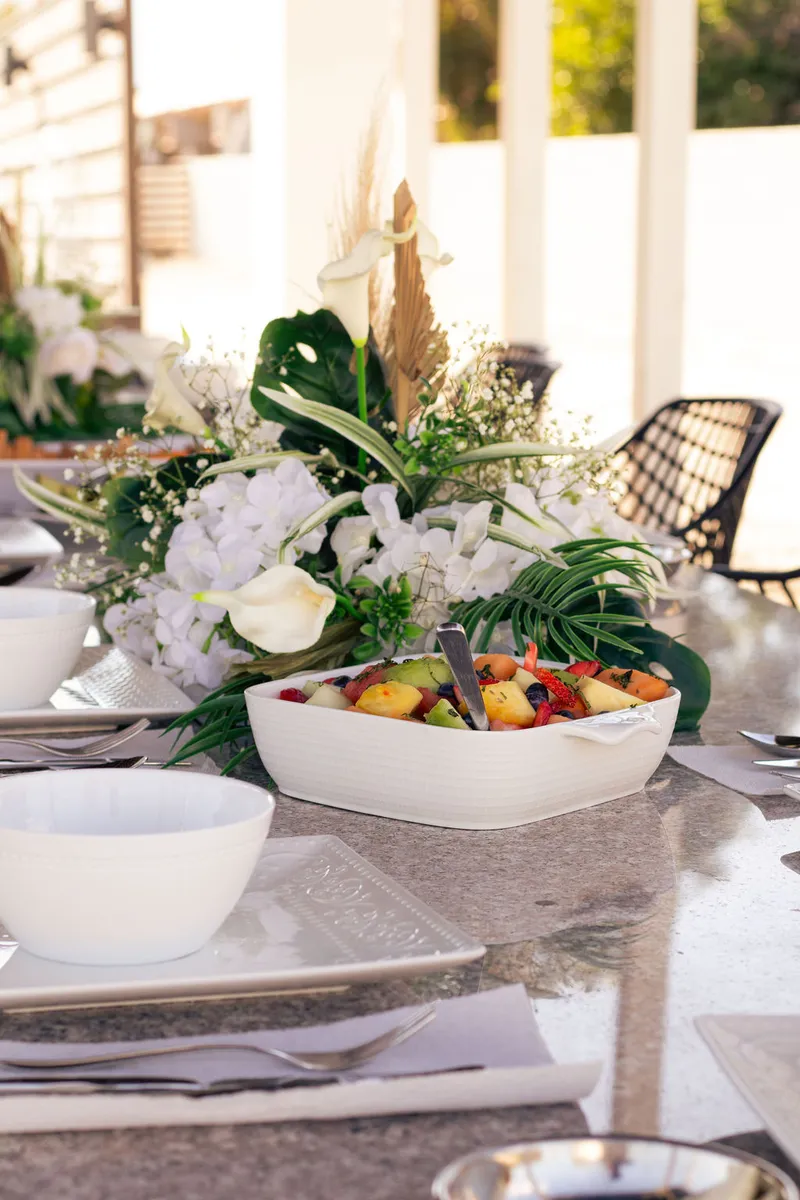 A daylight table with white florals, palm leaves and a bowl of fresh fruit