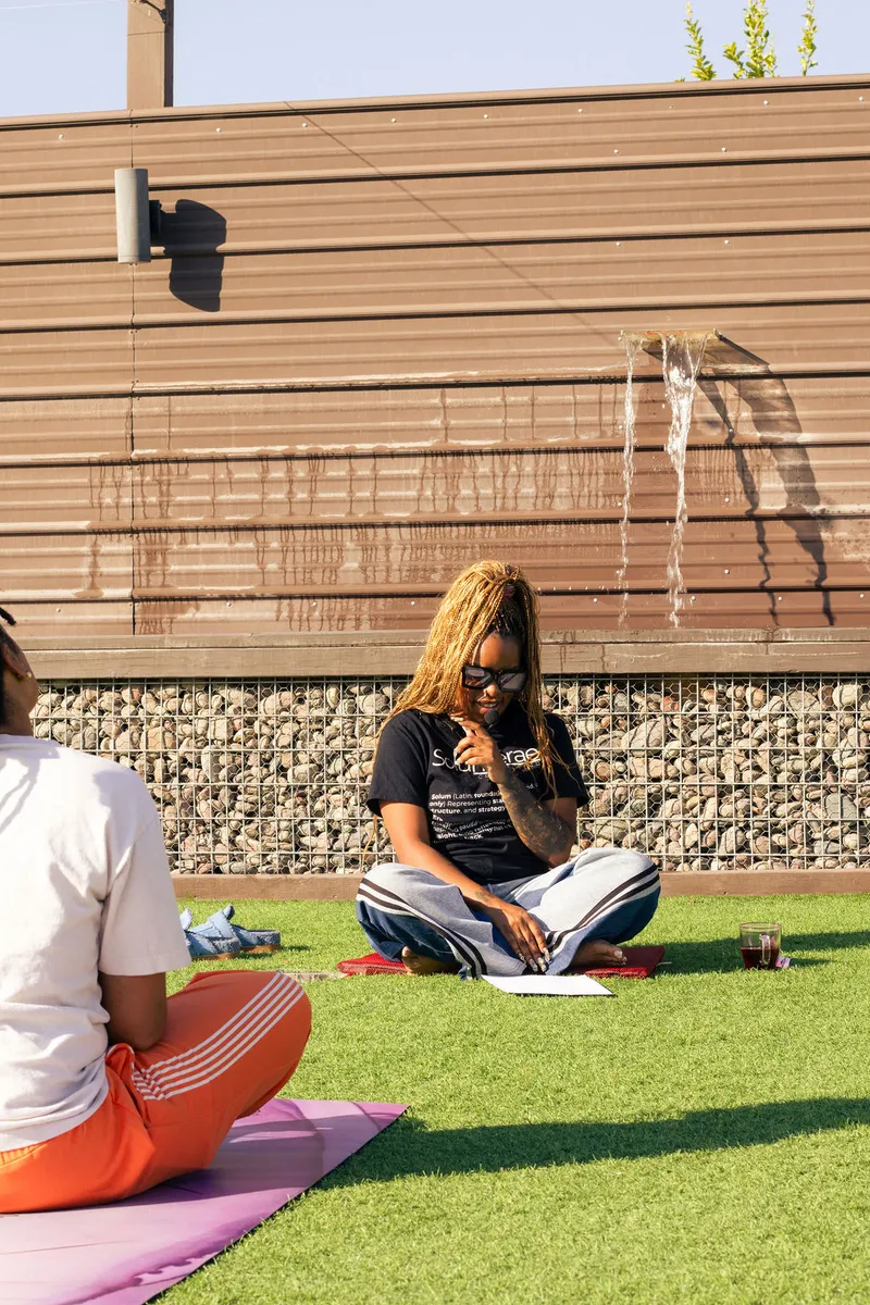 Two women sitting cross-legged on the grass in conversation during a golden-hour session