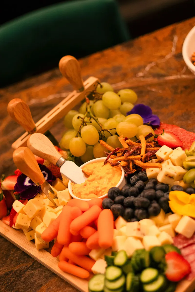 A wooden board loaded with grapes, berries, cheeses, carrots and edible flowers at a Solumere gathering