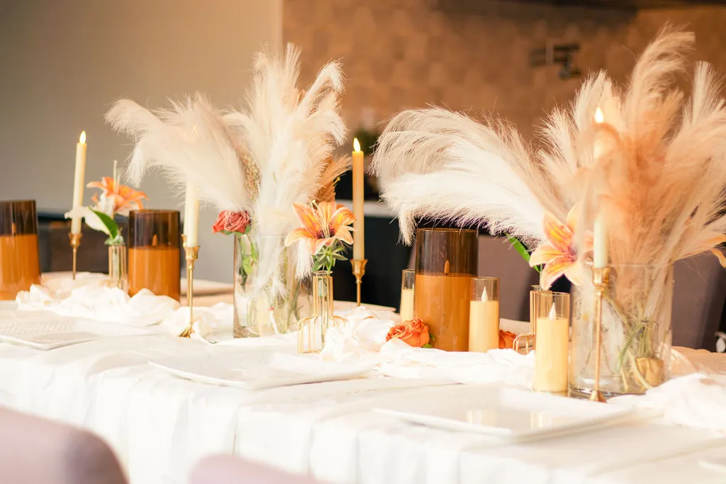 A long table lined with taper candles, pampas grass and orange lilies