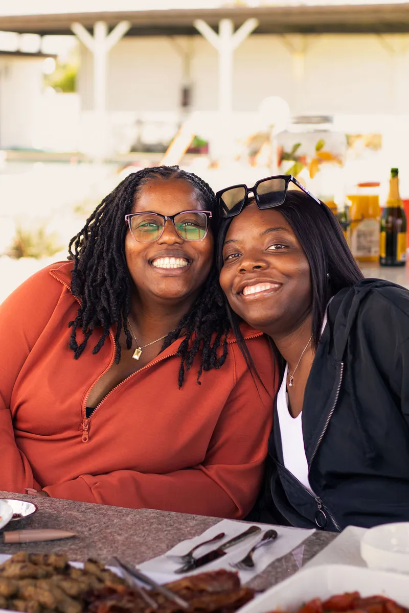 Two women leaning cheek to cheek, smiling at a brunch table set with plates and platters
