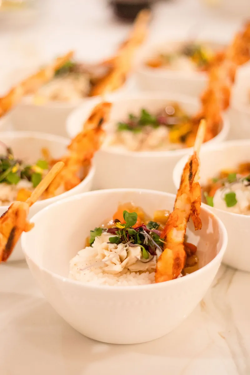Small white bowls plated with crab, rice and crisped shrimp on a marble counter